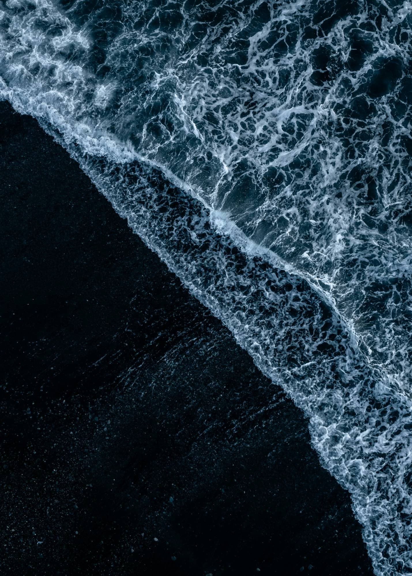 Surf breaking on a black sand beach, seen from above