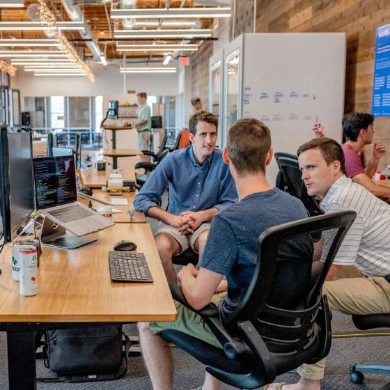 Three colleagues talking at a desk in an open-plan office